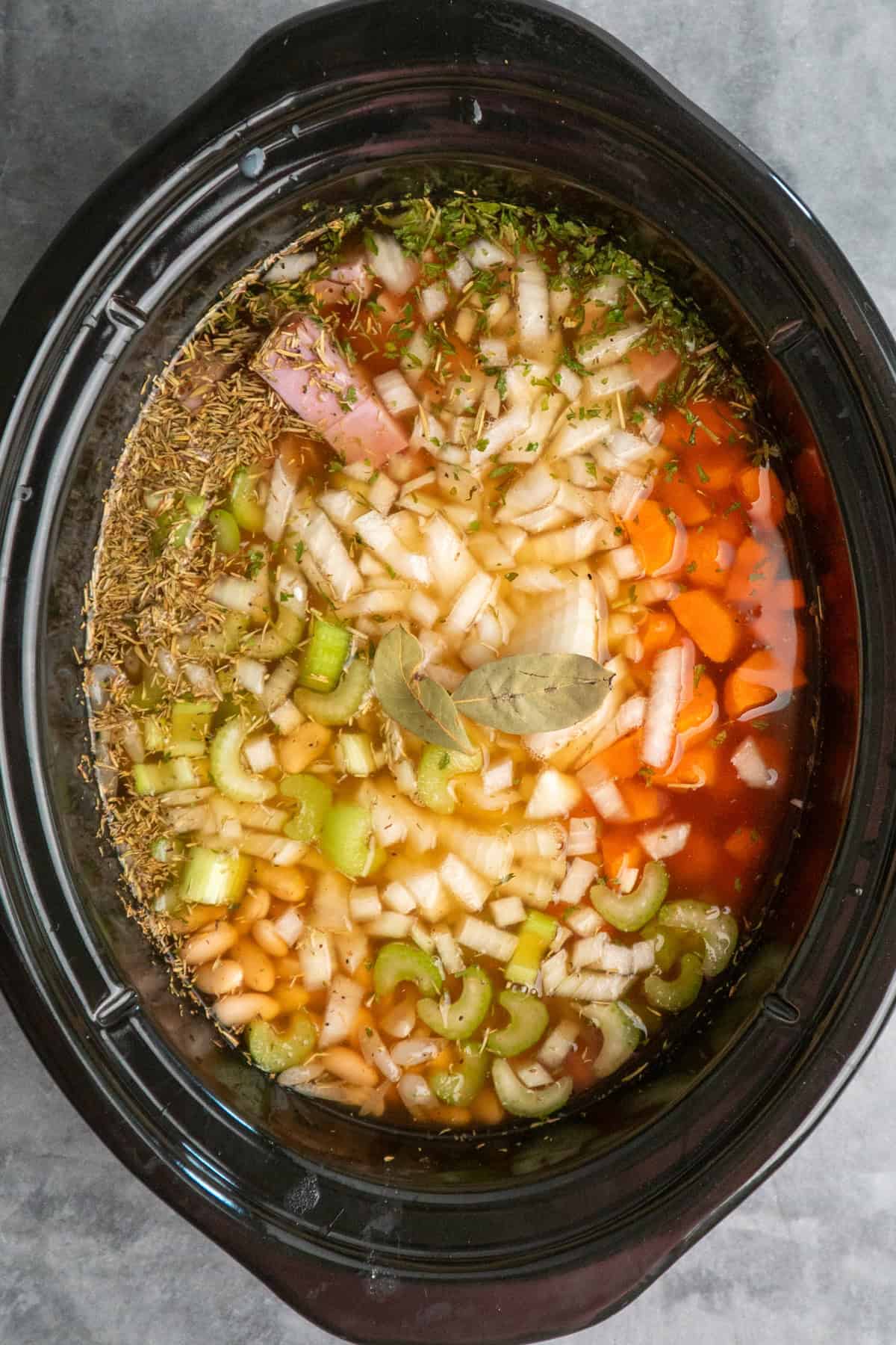 All the ingredients for ham and bean soup added to a slow cooker ready to be cooked.