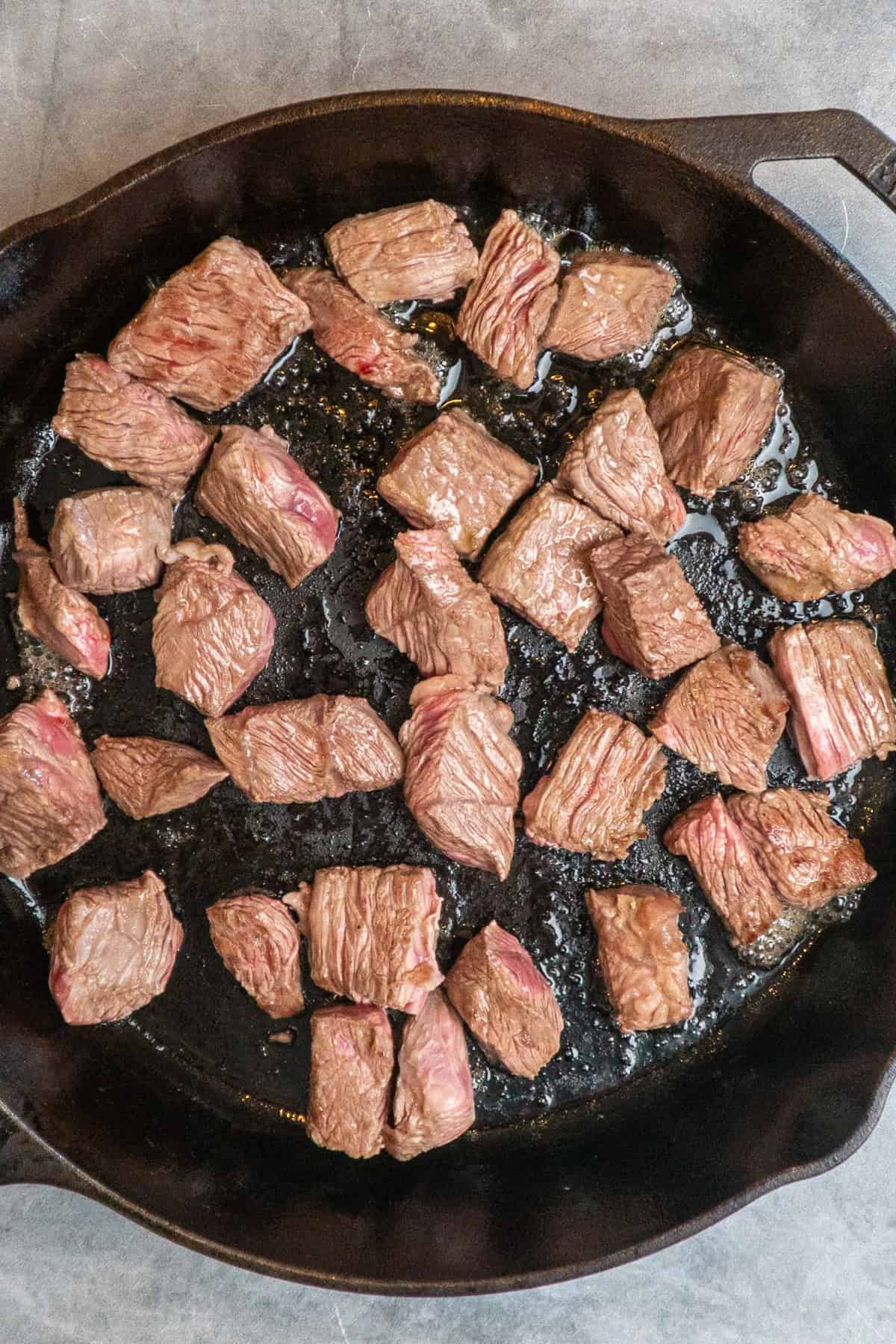 Chuck roast pieces seared in a cast iron skillet.