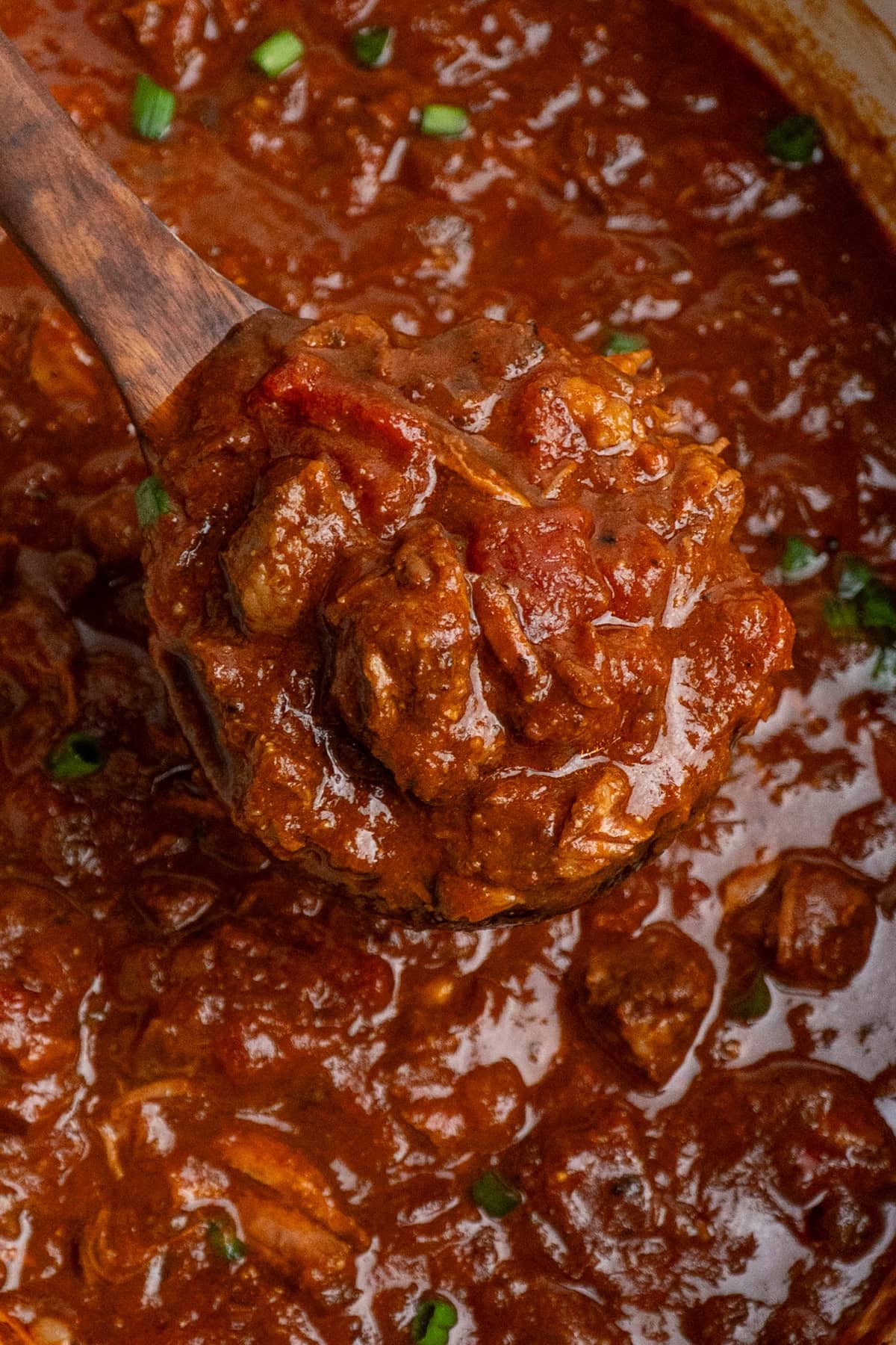 A wooden spoon holding  a scoop of Texas chili ready to be served.
