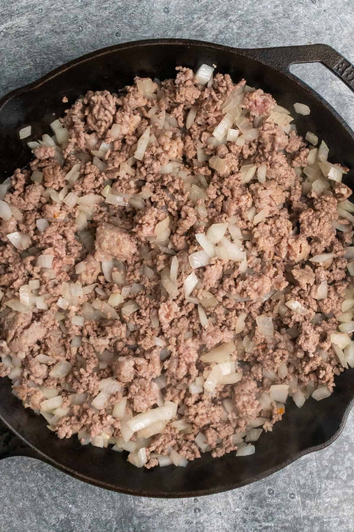 Ground beef, sausage, and onions cooking in a cast iron skillet.