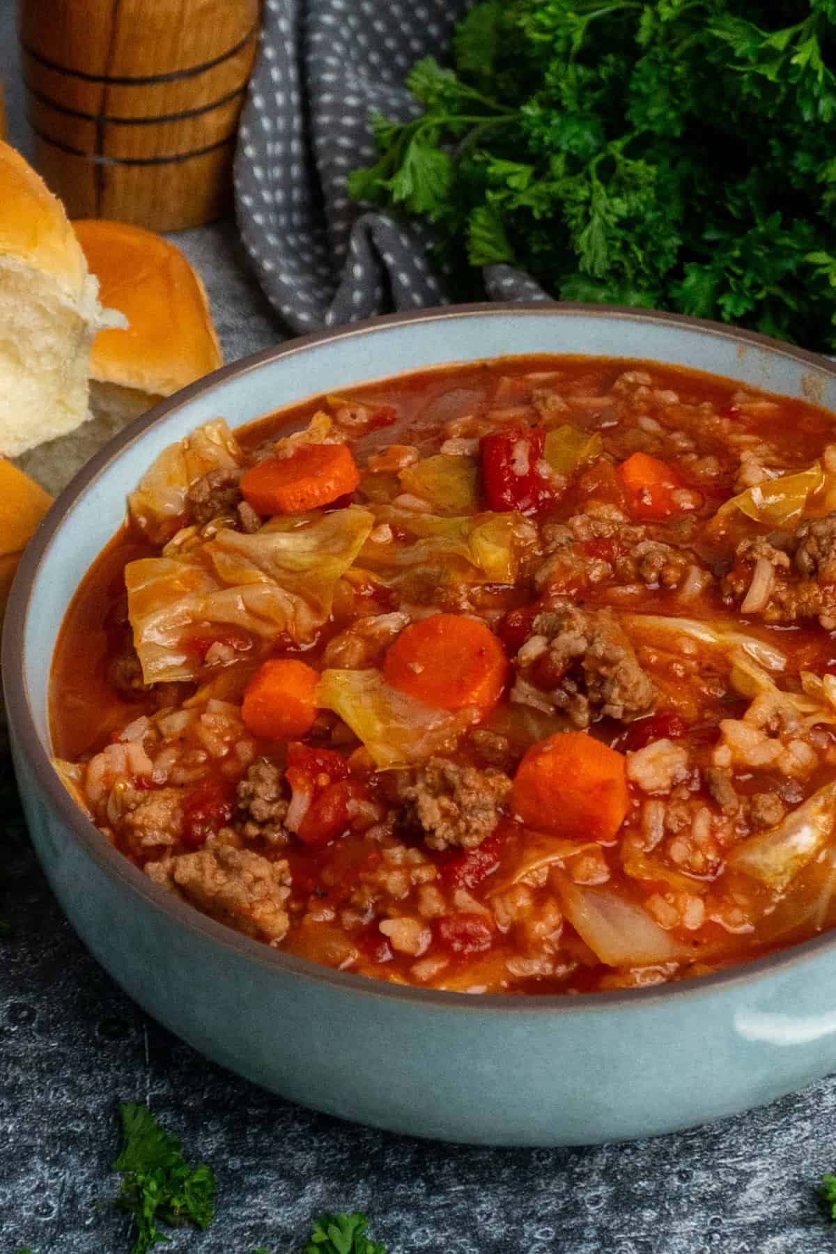 Cabbage roll soup in a bowl with rolls in the background.