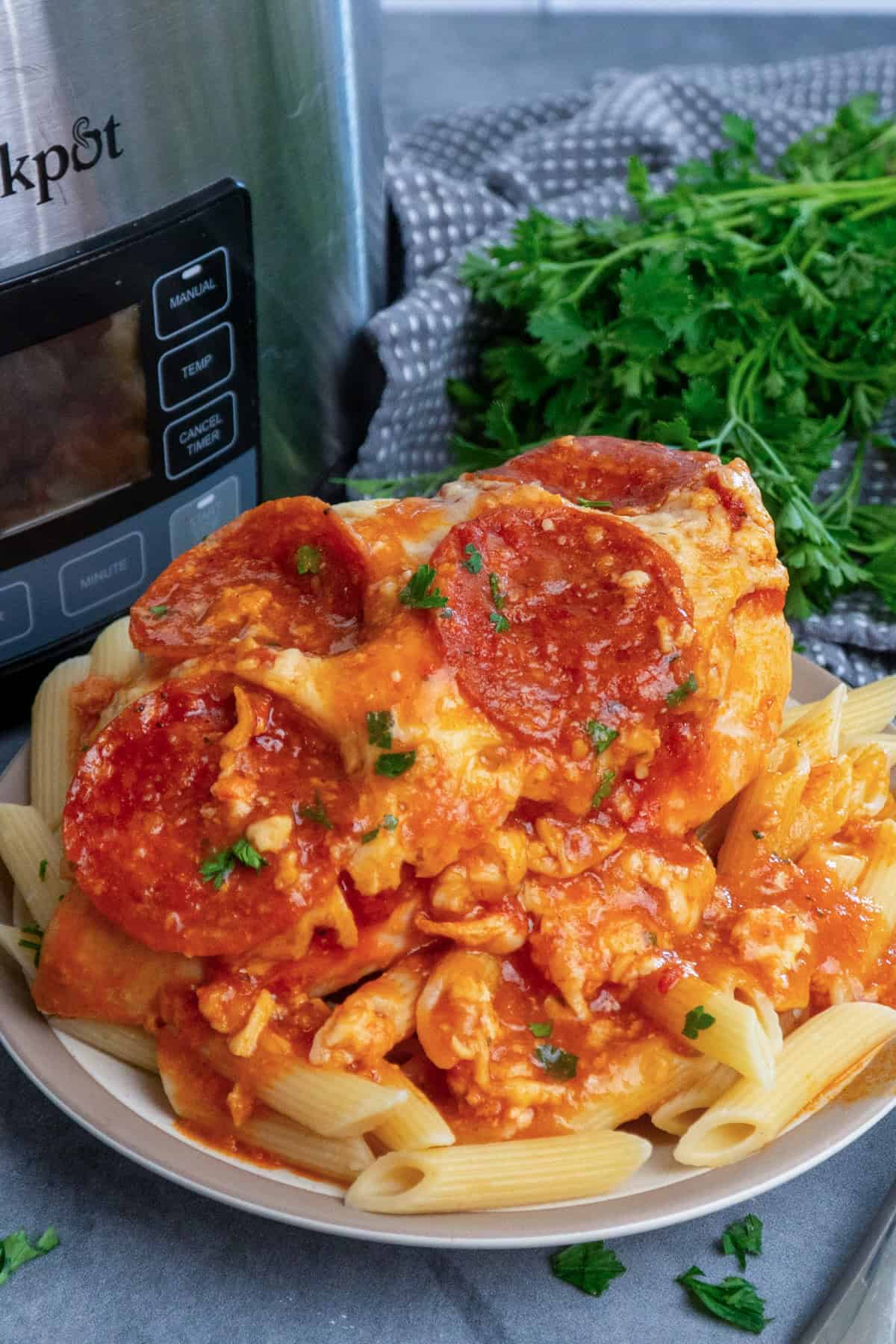 Slow cooker pizza chicken over a plate of pasta.