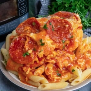 Slow cooker pizza chicken over a plate of pasta.