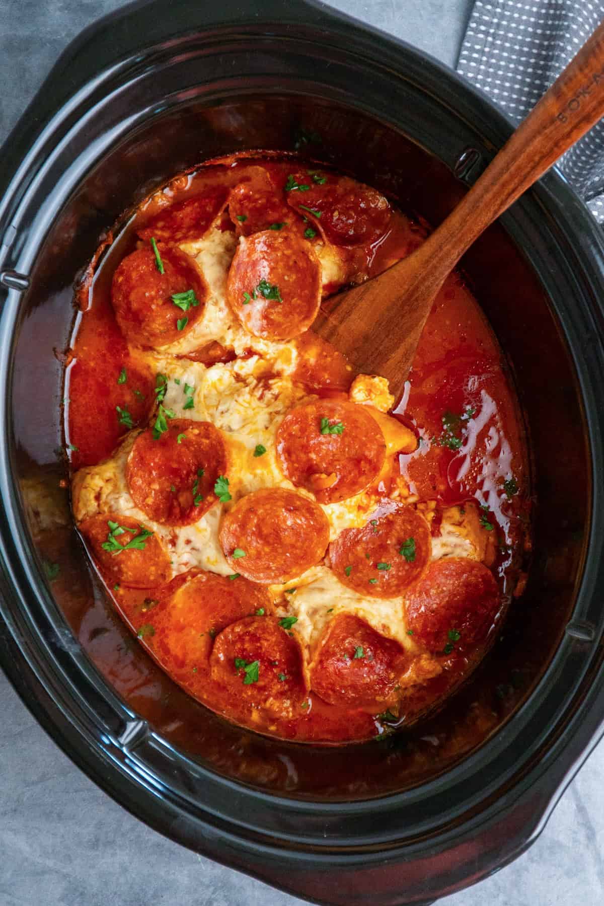 Slow cooker pizza chicken with a wooden spoon ready to be served.
