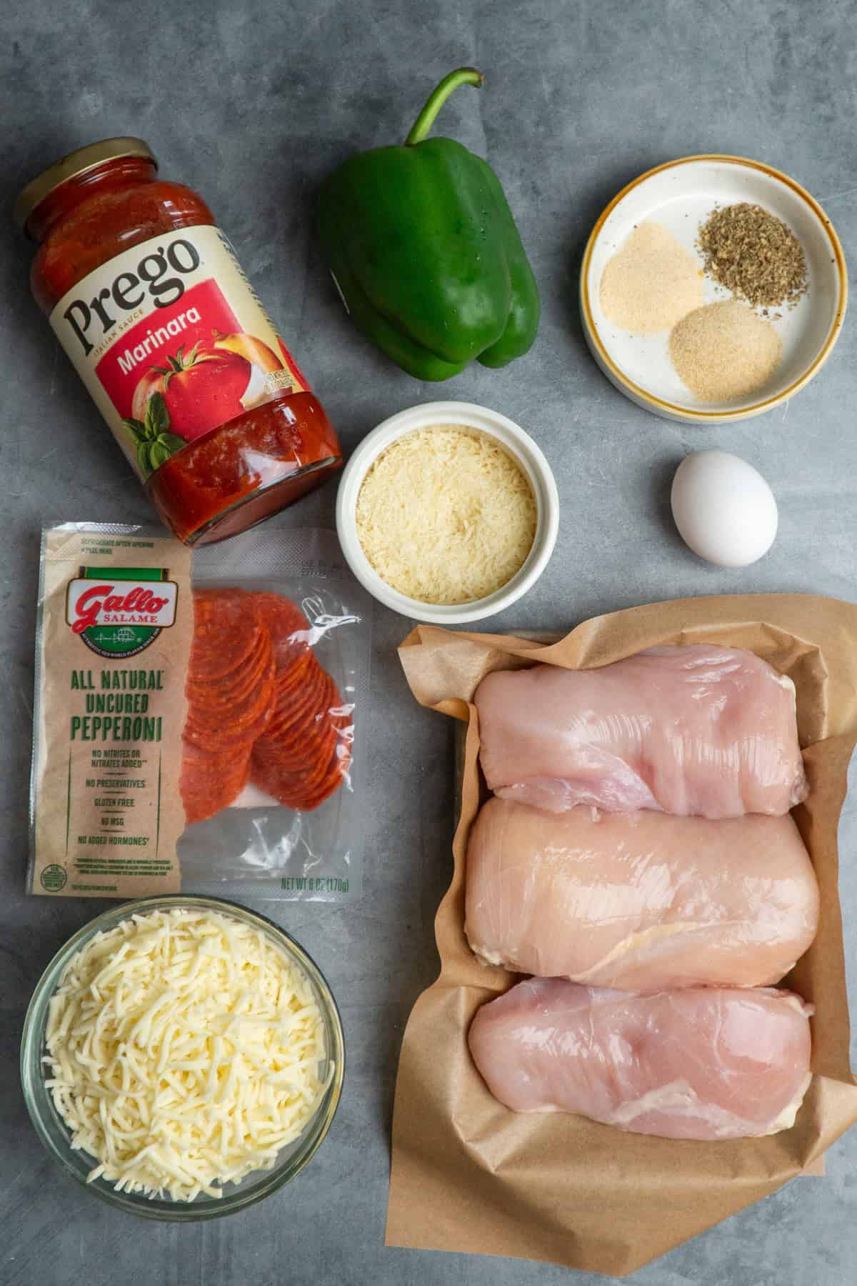 All the ingredients needed to make pizza chicken on a gray countertop.