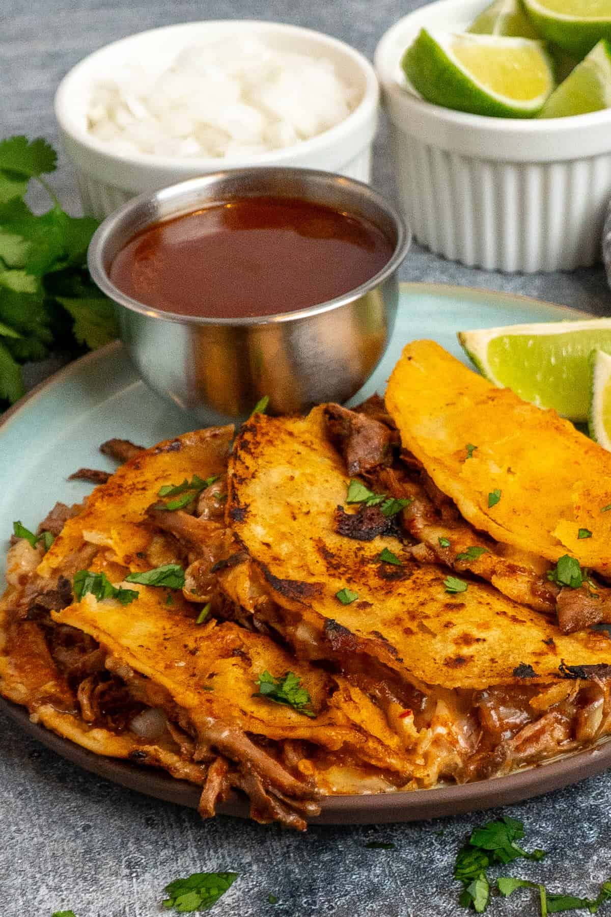 Three crock pot birria tacos on a plate with a bowl of broth.
