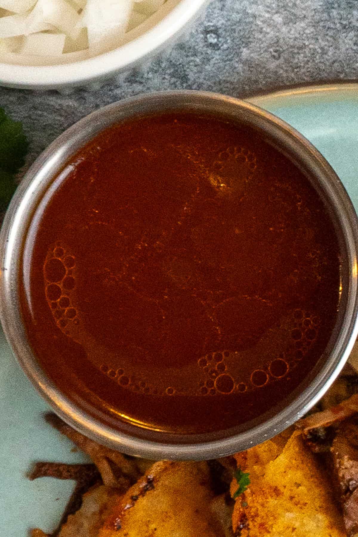 A bowl of strained birria consume in a metal bowl.