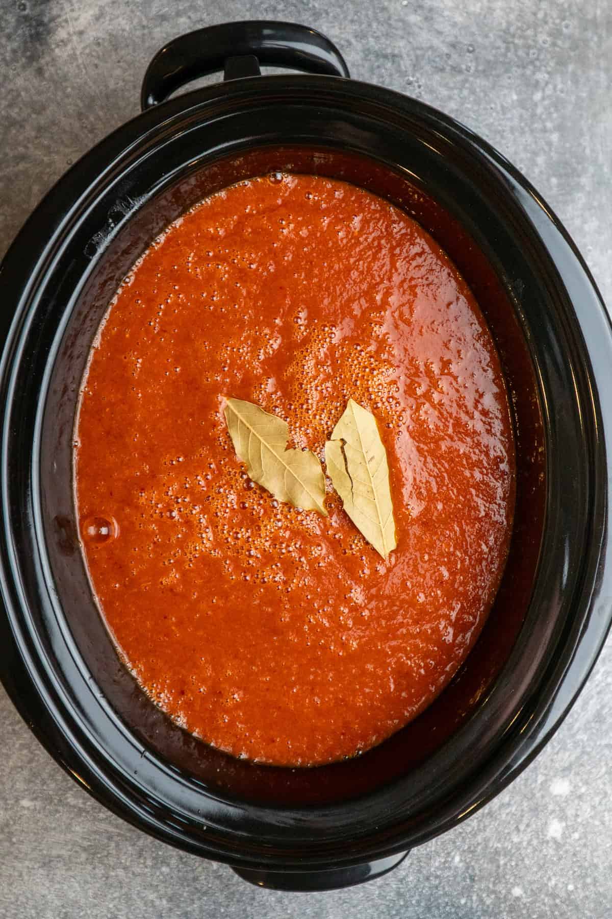 Chuck roast in a crock pot covered in birria sauce and bay leaves.