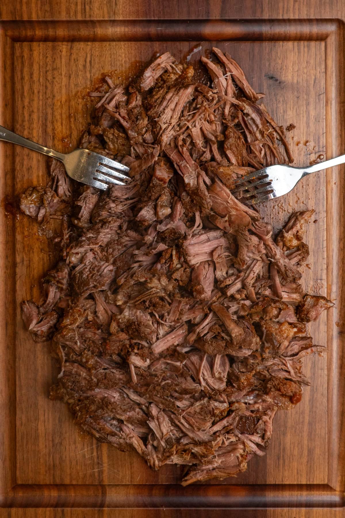 Cooked chuck roast shredded on a wooden cutting board.