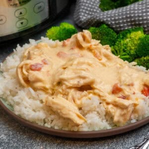 Cheesy chicken over a plate of rice with broccoli.