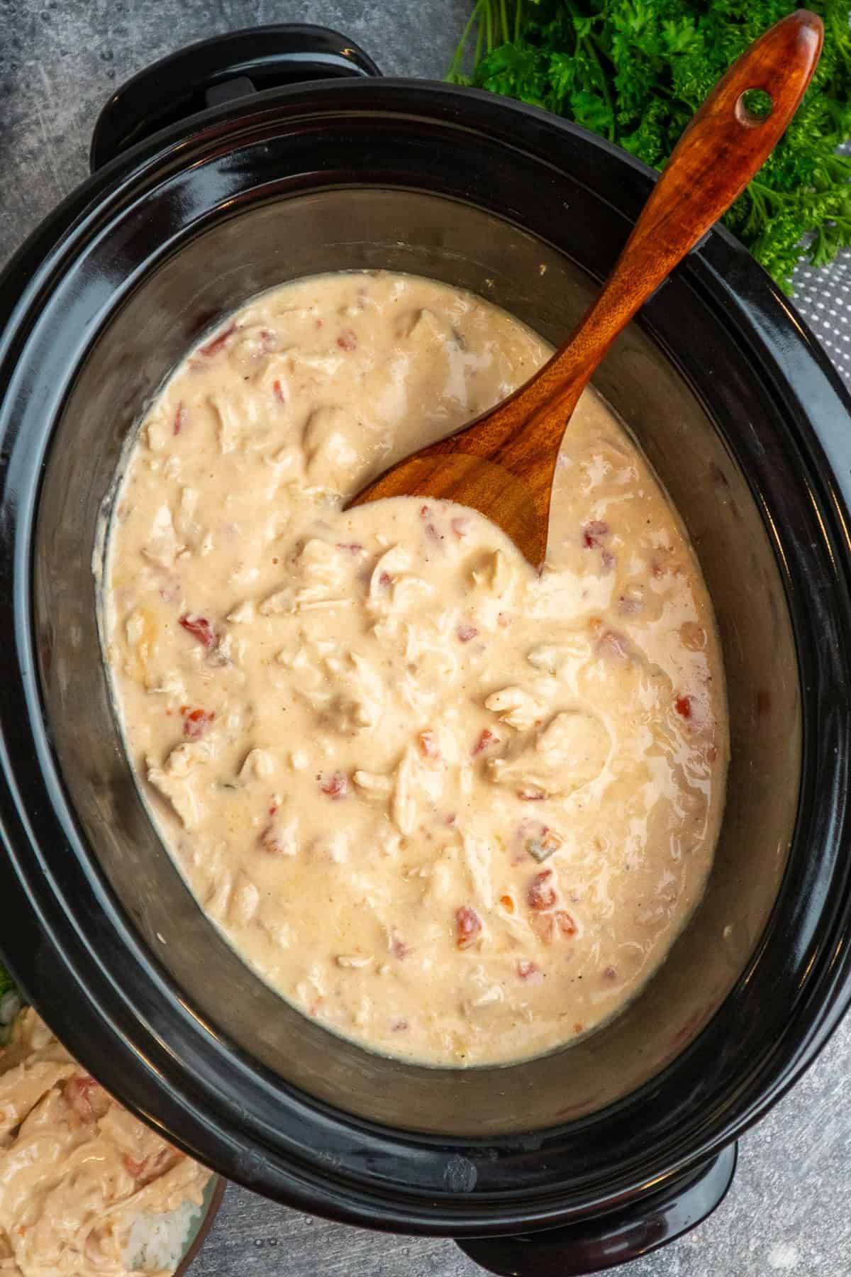 Crock pot cheesy chicken with a wooden spoon in it ready to be served.