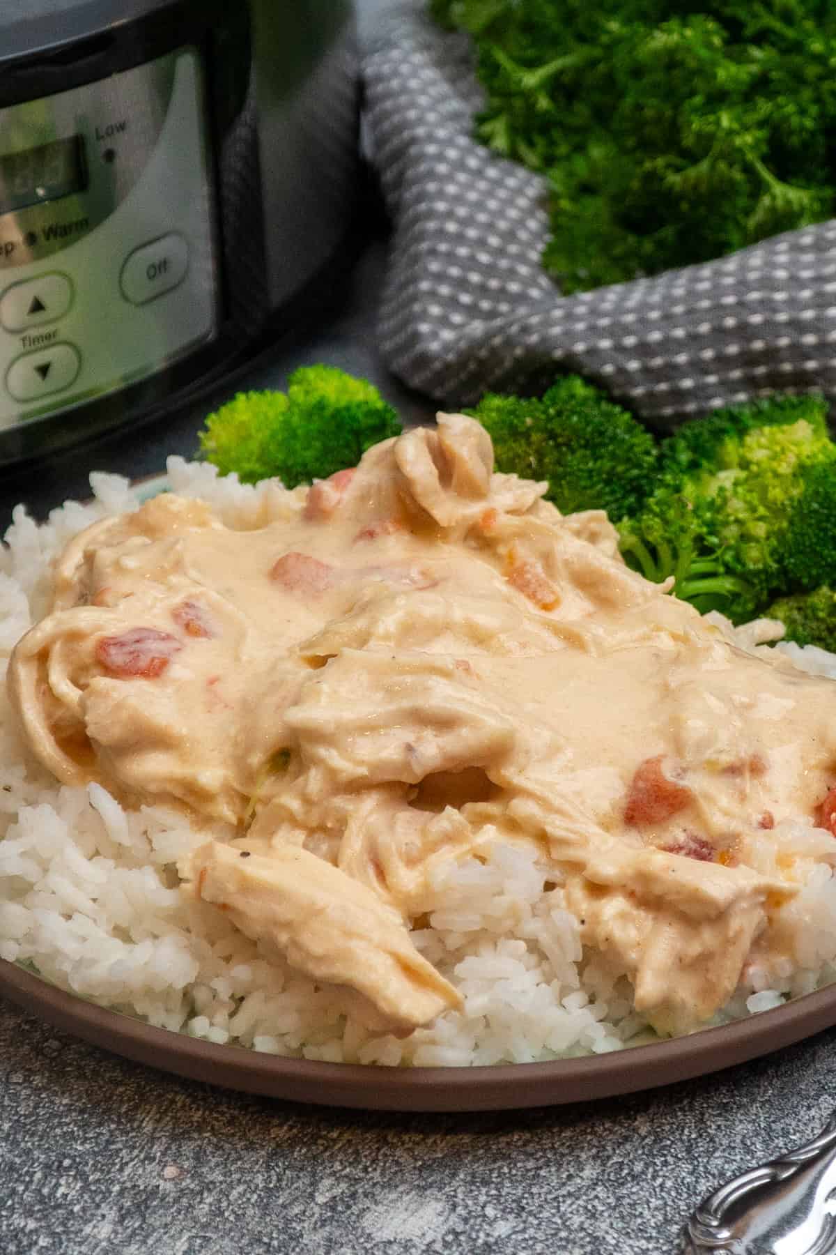 Cheesy chicken over a plate of rice with broccoli.