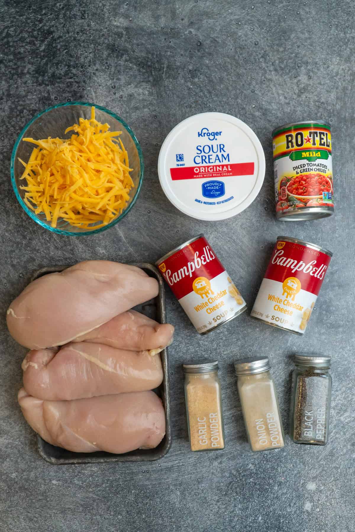 Ingredients to make cheesy chicken on a gray stone countertop.
