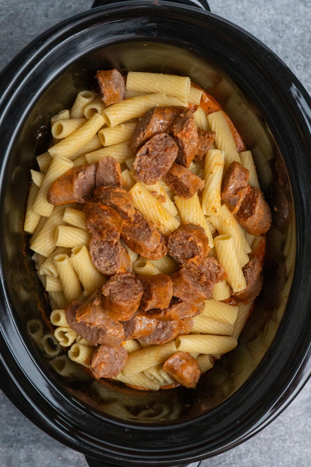 Pasta and Italian sausage added to the crock pot ready to have cheese put on top.