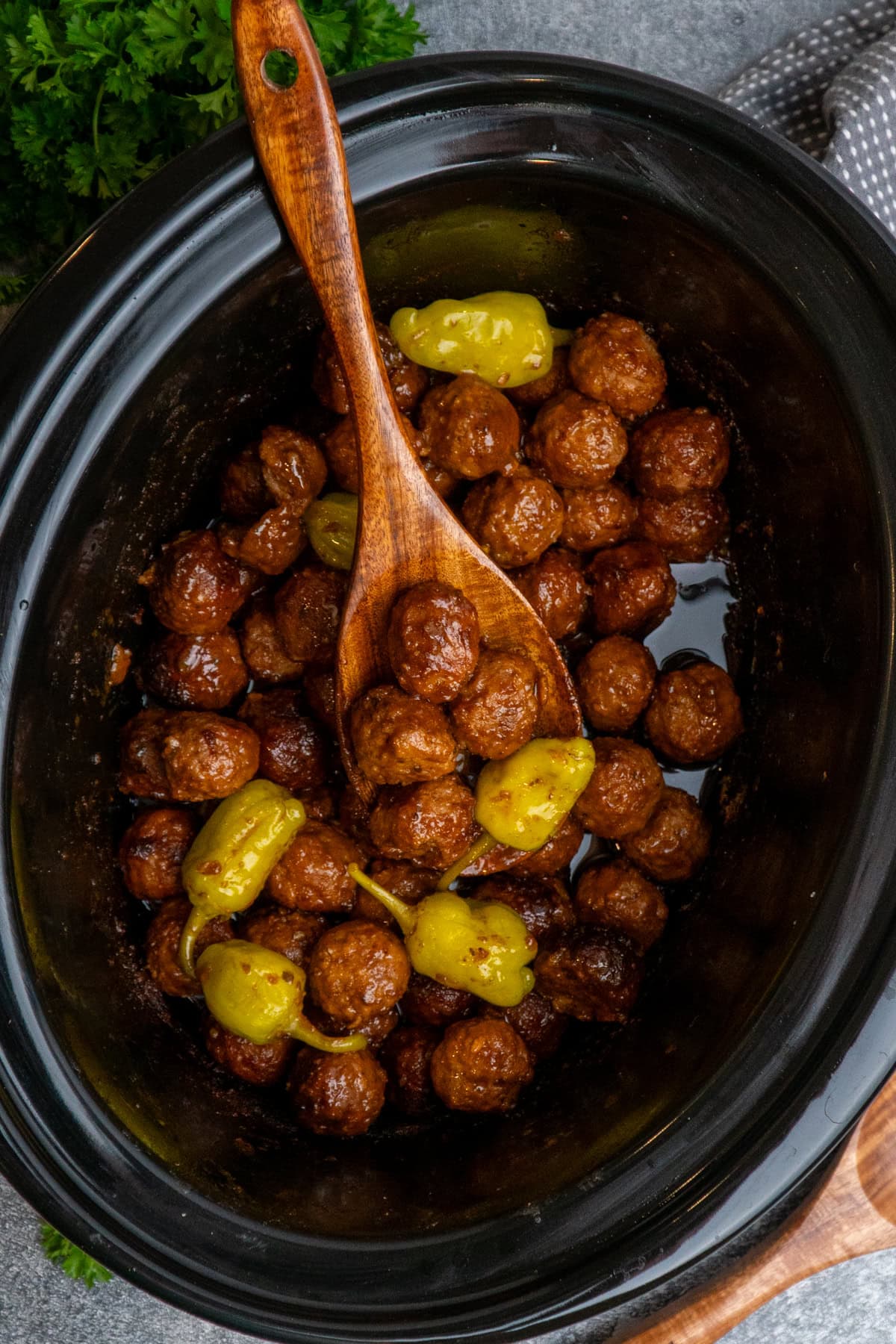 Cooked Mississippi meatballs in a crock pot with a wooden spoon holding a scoop of them.
