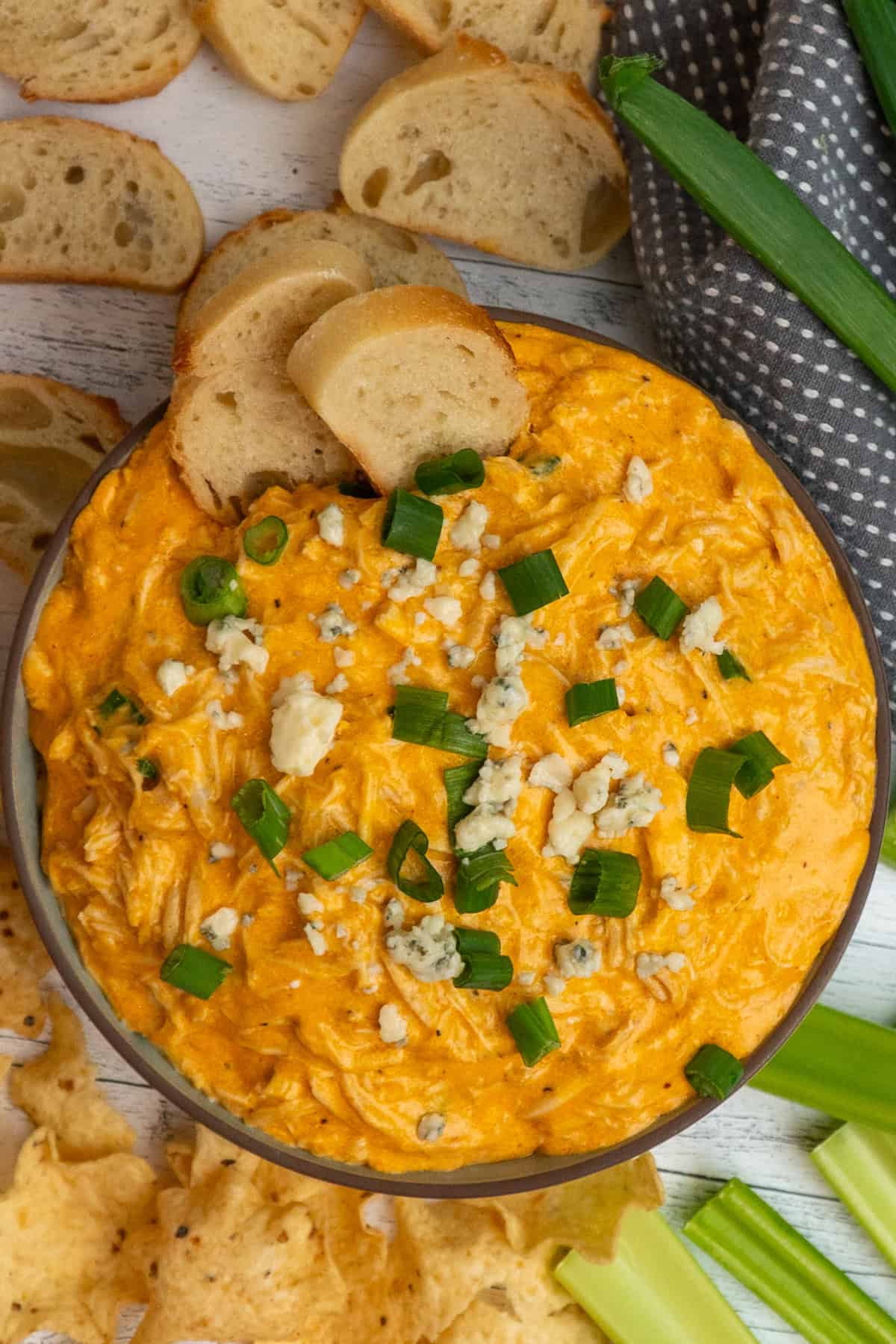Buffalo chicken dip in a bowl and surrounded by sliced baguettes, chips and celery.