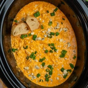Crock Pot buffalo chicken dip garnished with green onions and blue cheese crumbles.