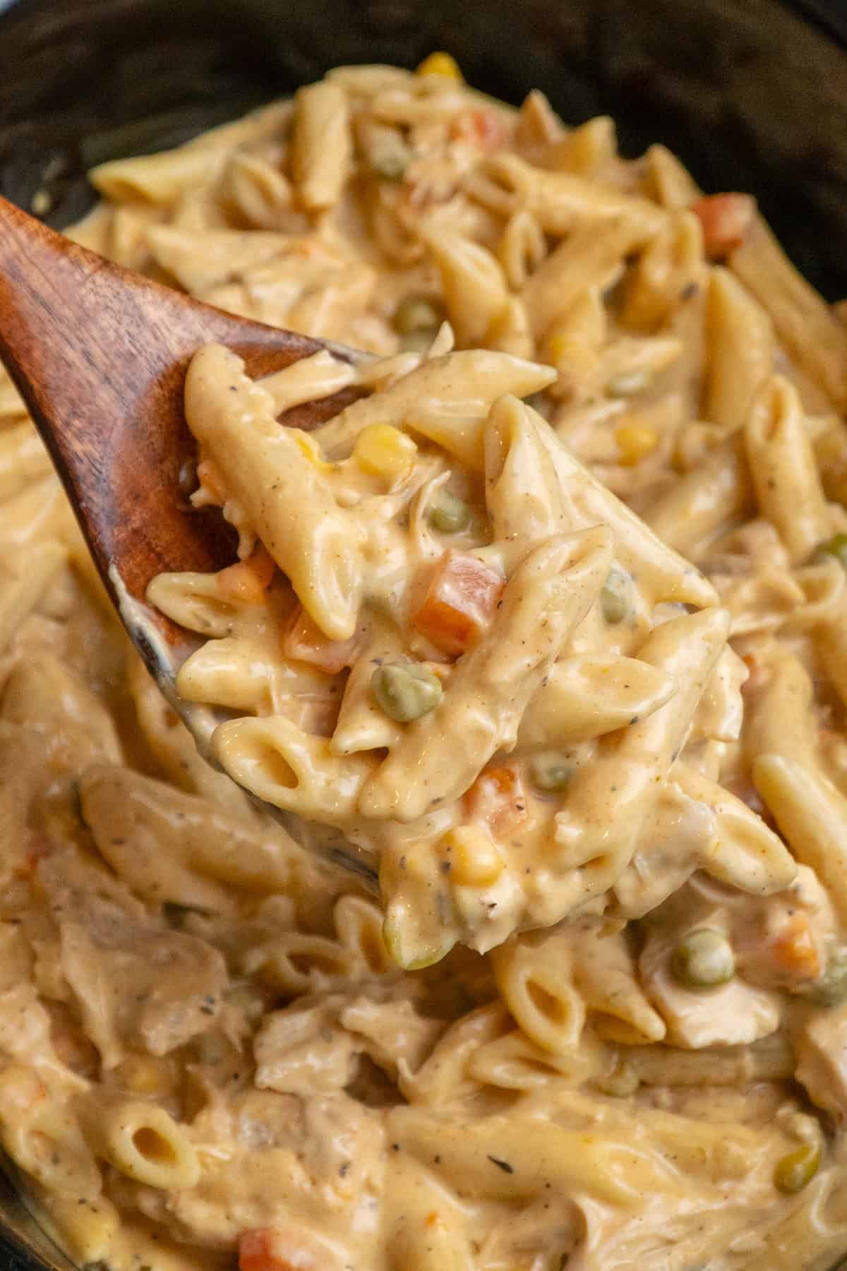 A wooden spoon picking up some pasta with chicken pot pie.