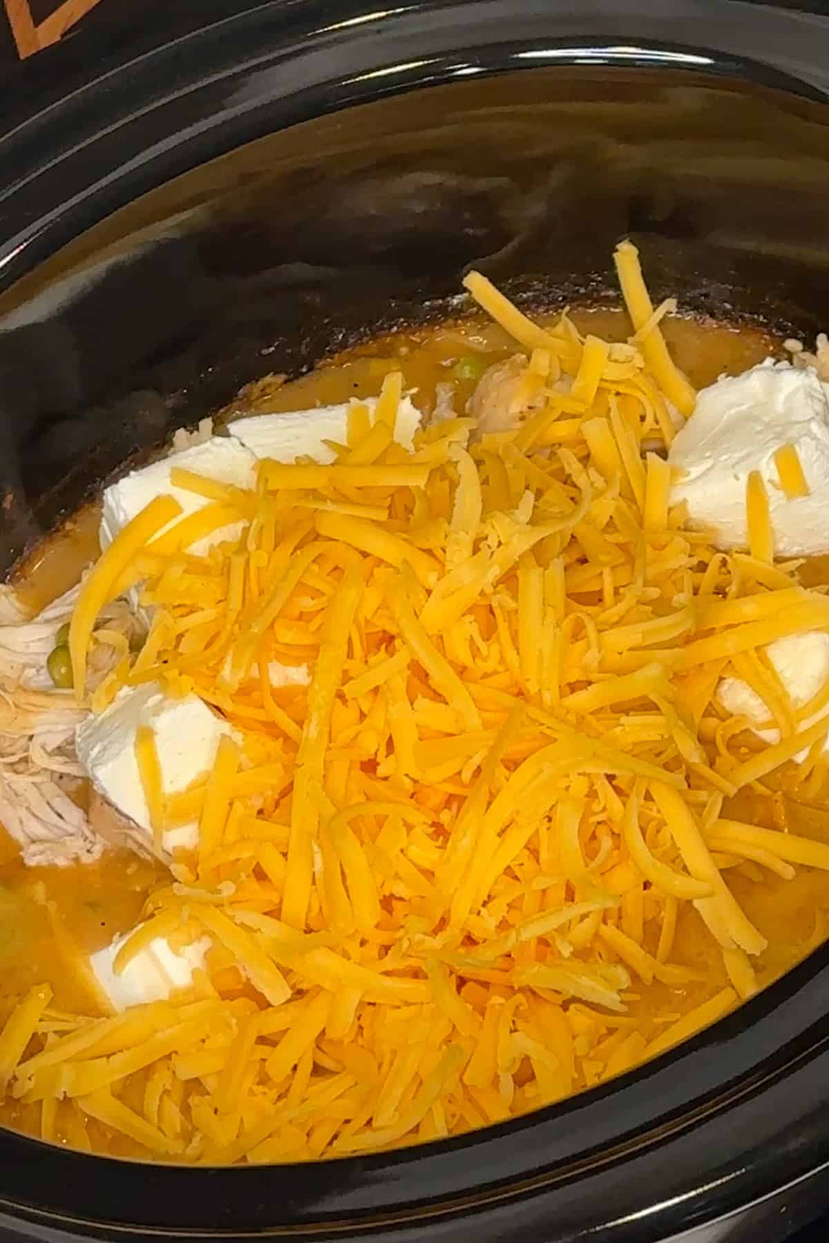 Shredded chicken, cream cheese, sour cream and grated cheddar cheese added to the sauce in the crock pot.