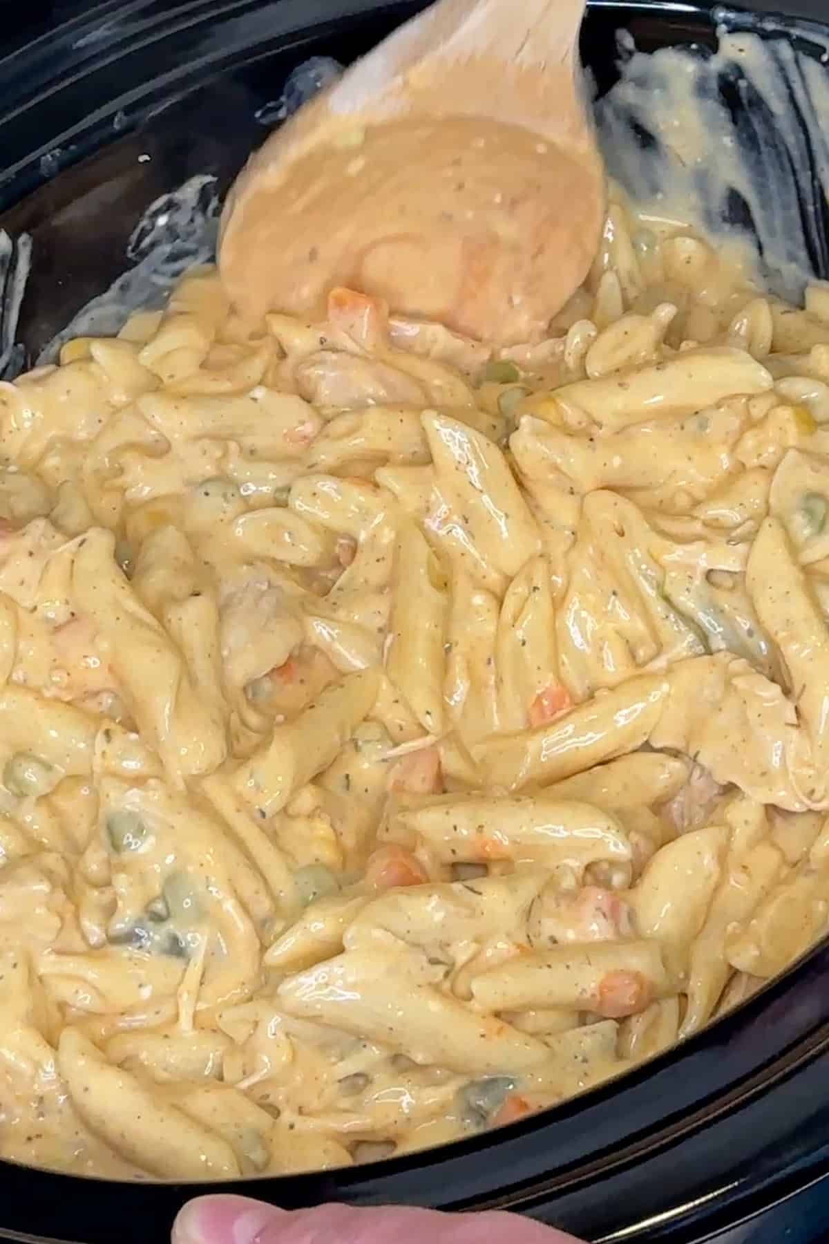 Cooked penne pasta getting mixed into the sauce and shredded chicken.