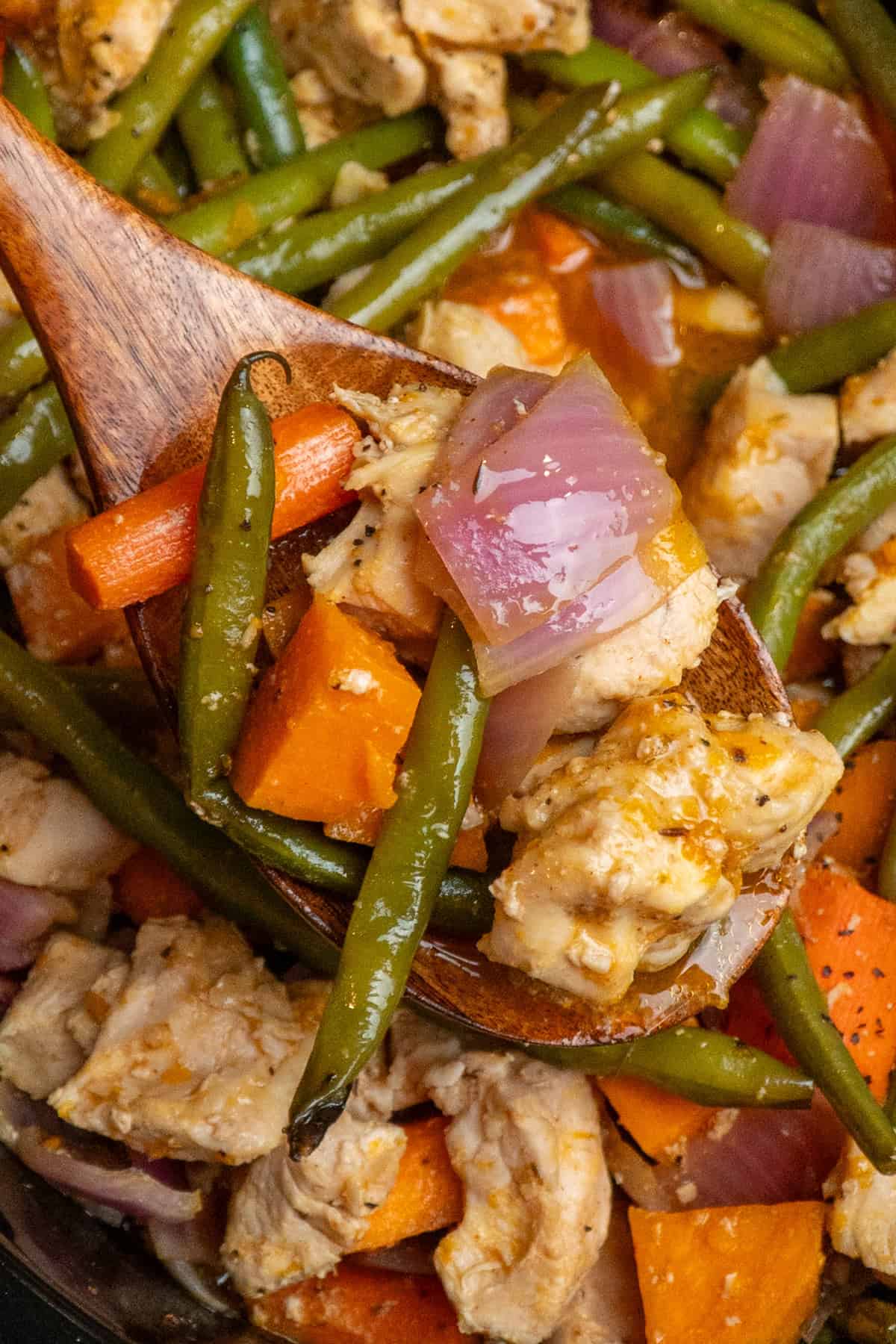 A wooden spoon holding a scoop of chicken and vegetables.