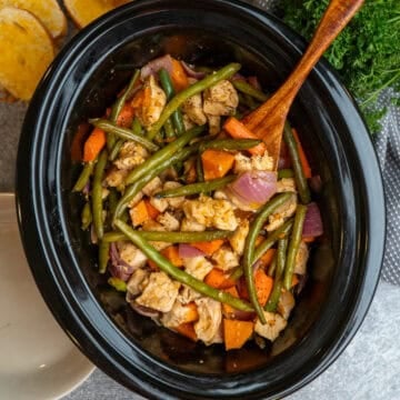 Crock Pot chicken and veggies with a wooden spoon in it ready to be served.