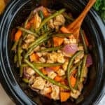 Crock Pot chicken and vegetables with a wooden spoon in it ready to be served.