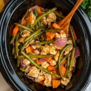 Crock Pot chicken and vegetables with a wooden spoon in it ready to be served.