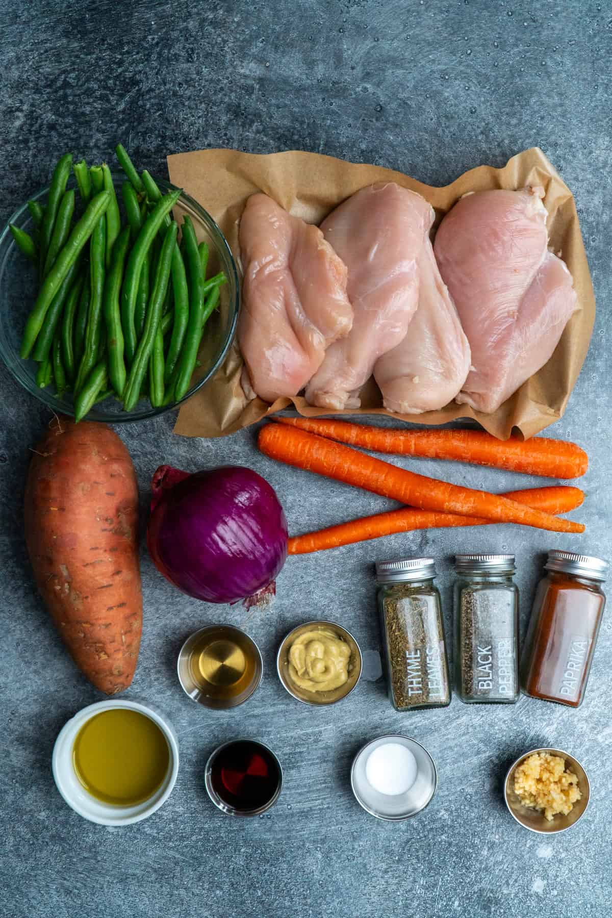 Ingredients to make chicken and vegetables on a gray stone counterop.