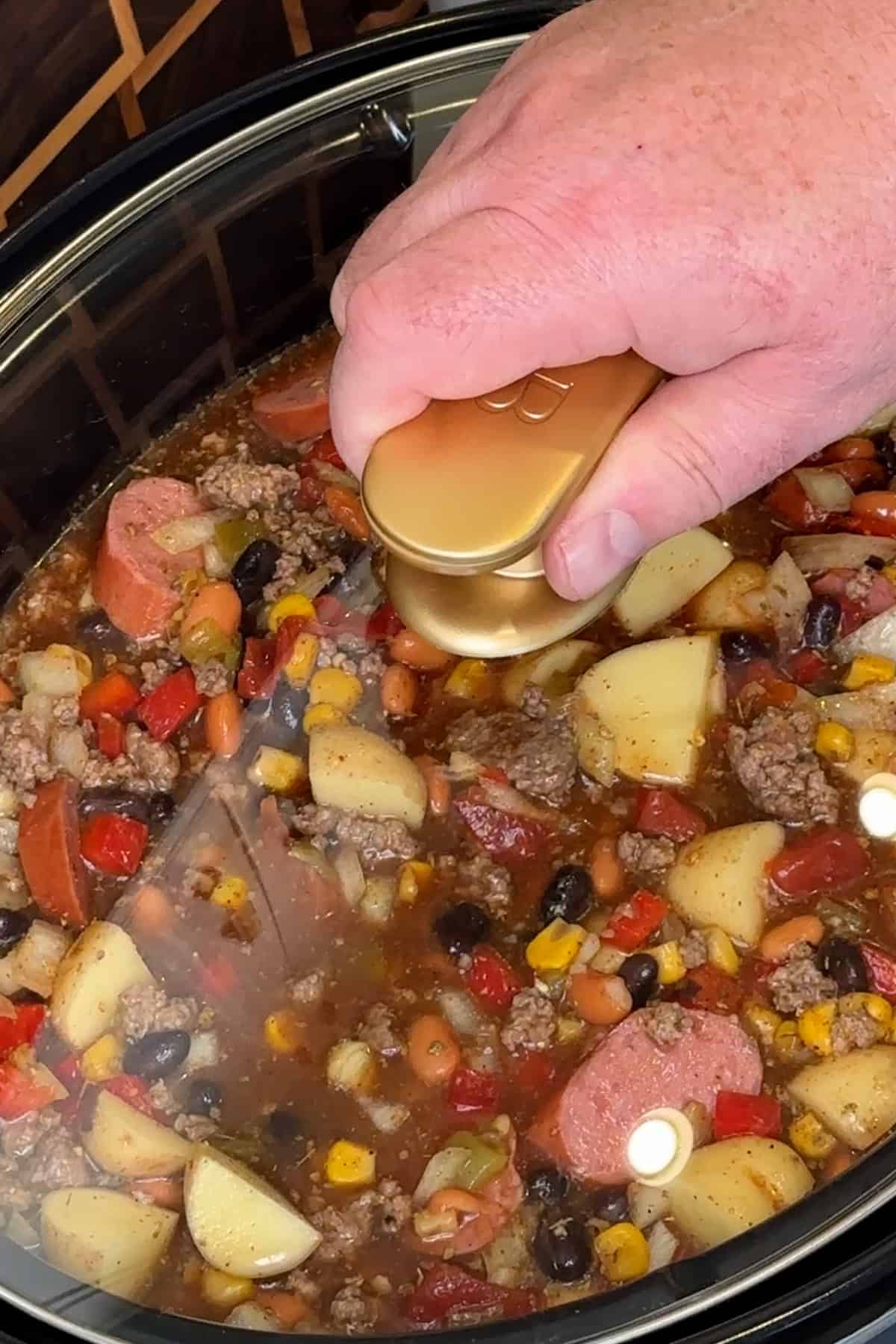 A hand putting the lid on a crock pot so the cowboy soup can be cooked.