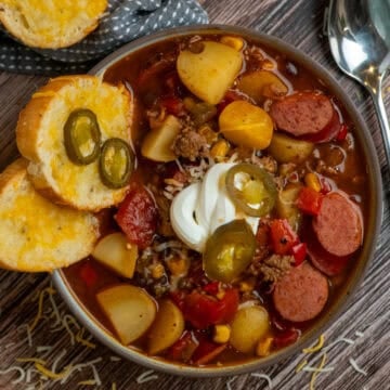 Cowboy soup in a bowl garnished with sour cream, jalapenos, and cheese bread.