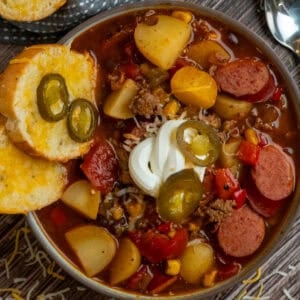 Cowboy soup in a bowl garnished with sour cream, jalapenos, and cheese bread.