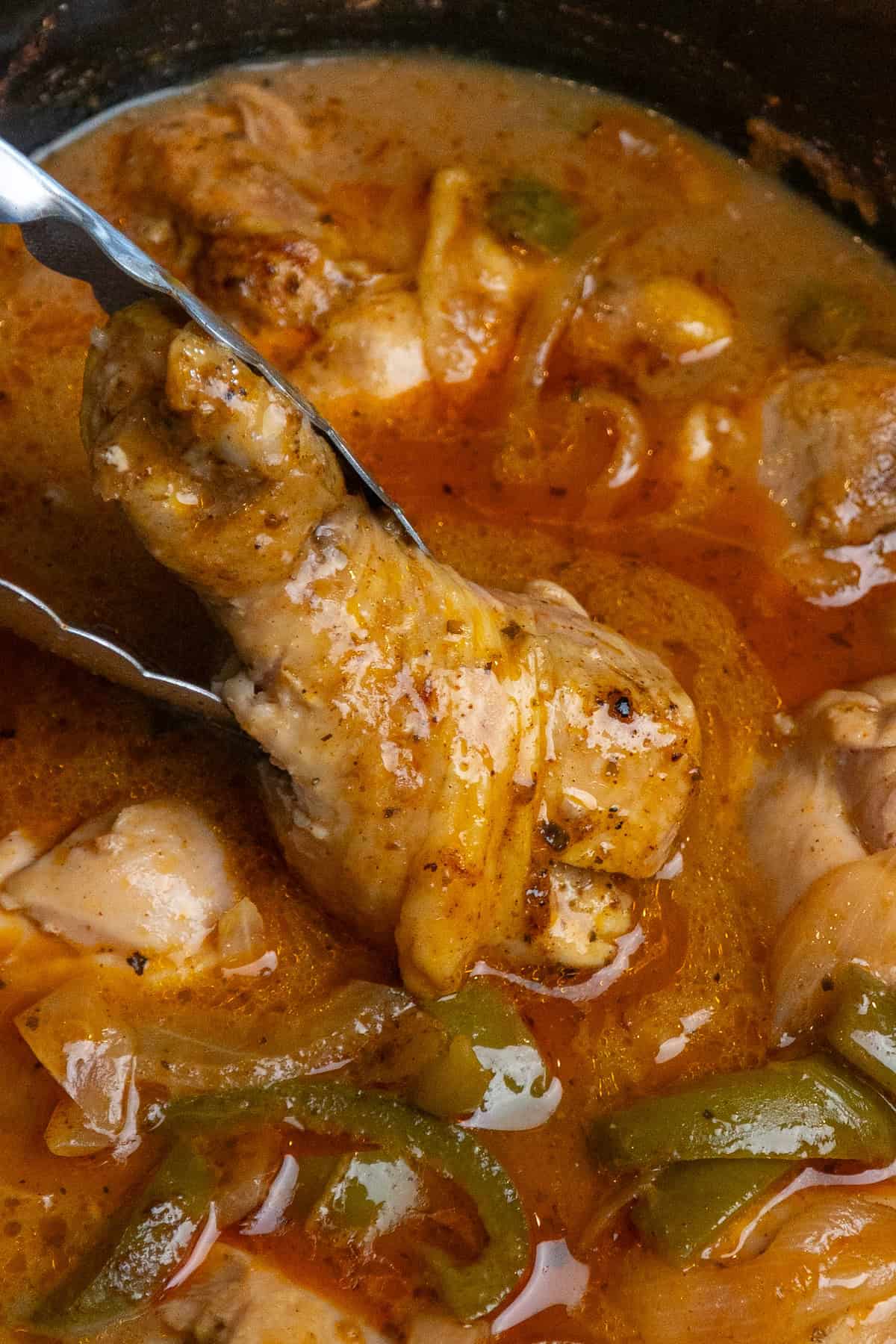 A smothered chicken leg being taken out of the crock pot.