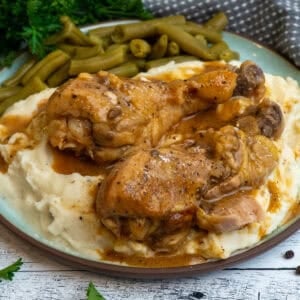 Crock Pot smothered chicken legs over a plate of mashed potatoes and green beans.