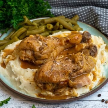Crock Pot smothered chicken legs over a plate of mashed potatoes and green beans.