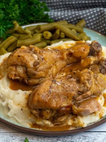 Crock Pot smothered chicken legs over a plate of mashed potatoes and green beans.