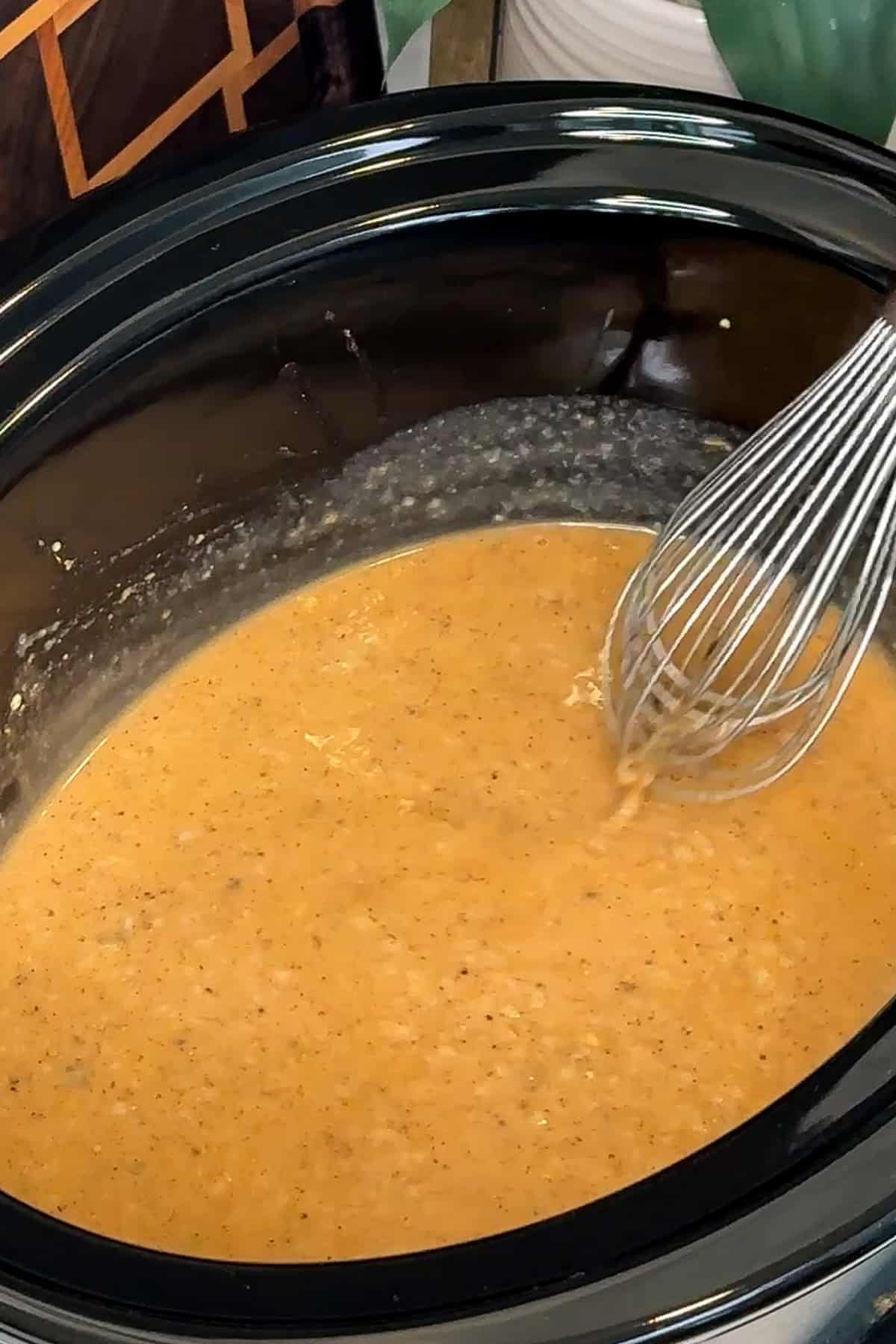 Chicken broth, gravy, seasonings, mushroom soup, Dijon mustard and Worcestershire sauce being whisked together in a crock pot.