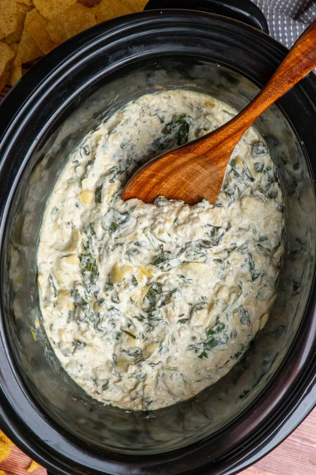 Crock Pot spinach artichoke dip with a wooden spoon ready to be served.