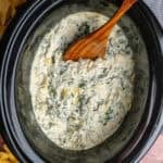 Crock Pot spinach artichoke dip with a wooden spoon ready to be served.