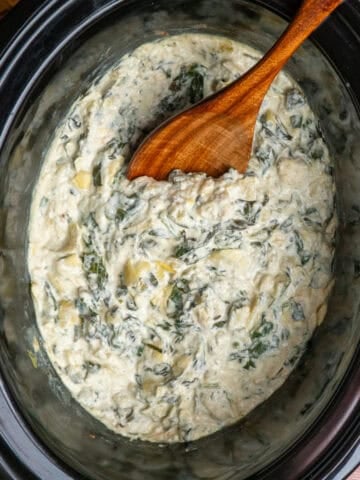 Crock Pot spinach artichoke dip with a wooden spoon ready to be served.