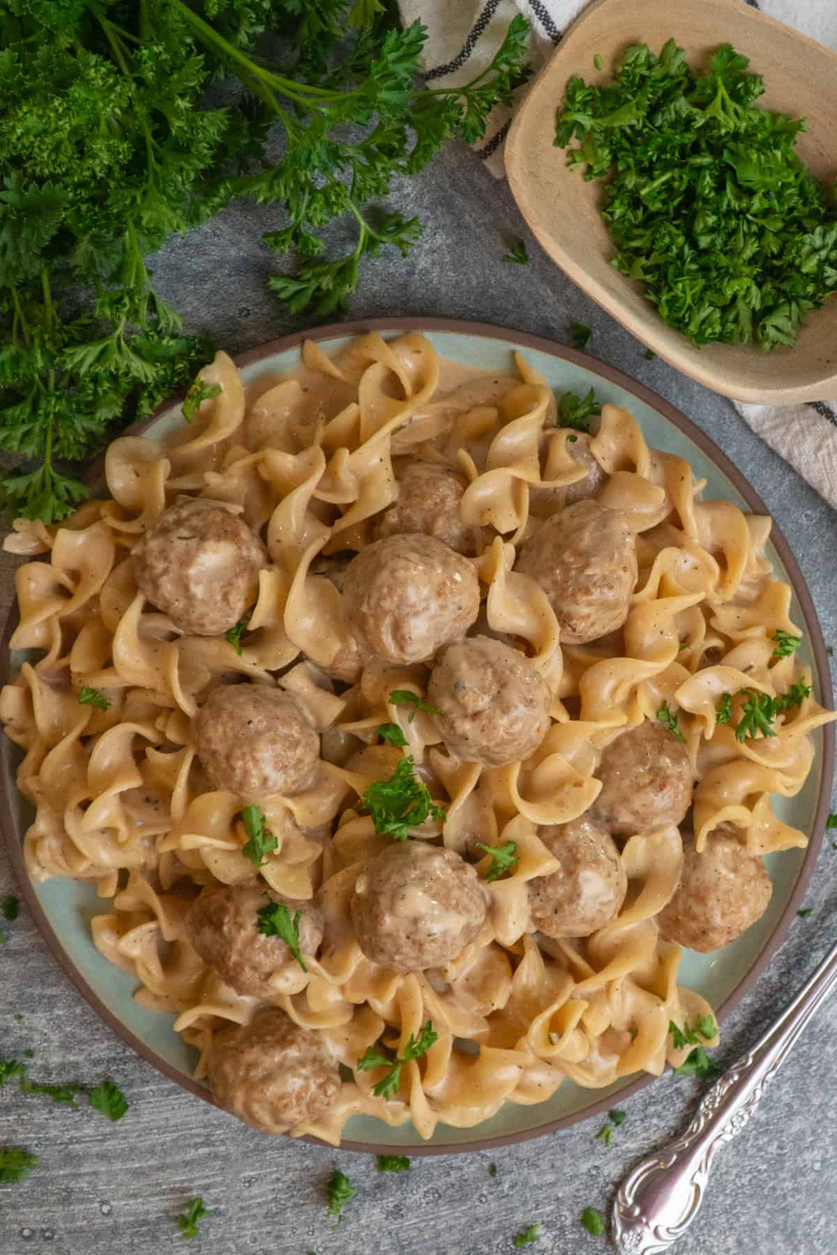 Swedish meatballs over a plate of noodles and garnished with fresh parsley.