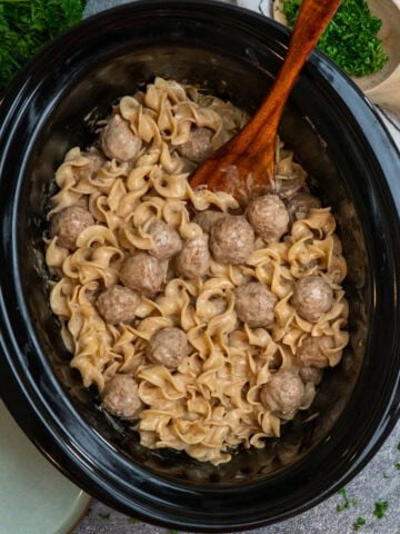 Crock Pot Swedish meatballs with a wooden spoon in it ready to be served.