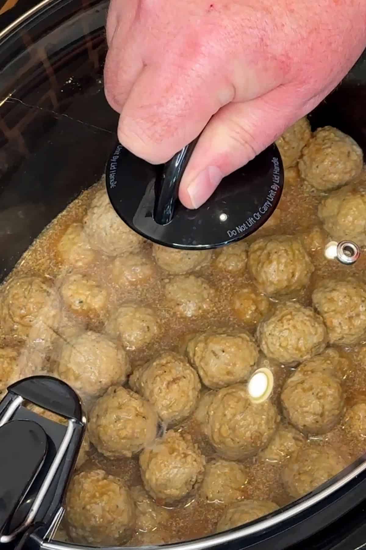 A hand putting the lid on the crock pot so the meatballs can be cooked.