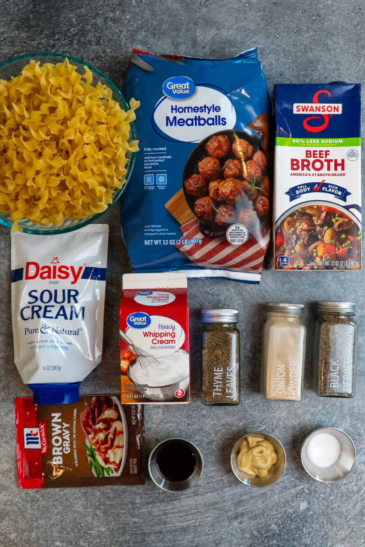 Meatballs, beef broth, egg noodles, sour cream, heavy cream, gravy, and seasonings on a gray stone counterop.