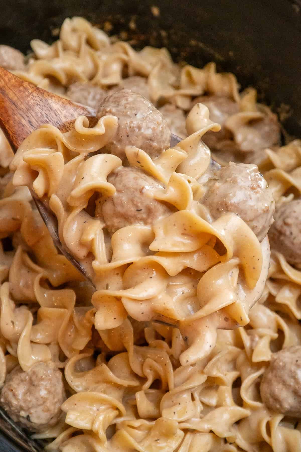 A wooden spoon holding Swedish meatballs over a crock pot.
