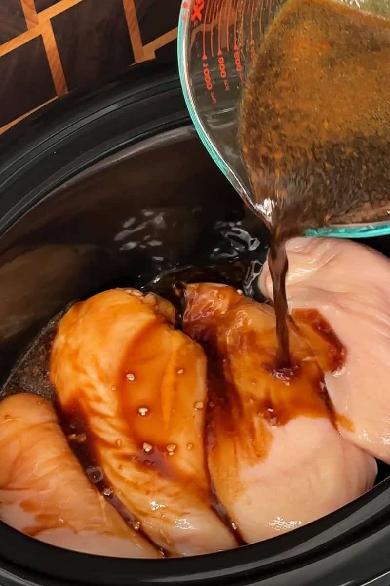Teriyaki sauce being poured over chicken breasts in a crock pot.