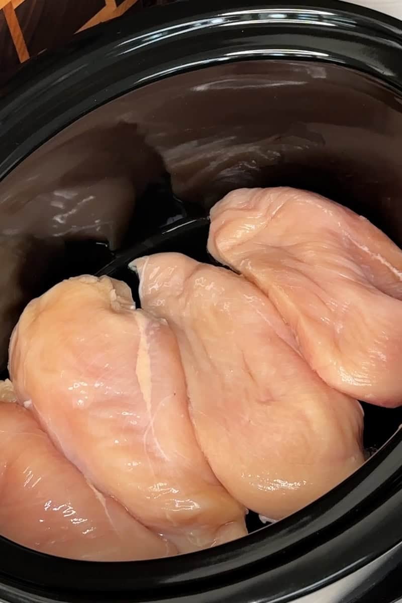 Four chicken breasts added to a crock pot.