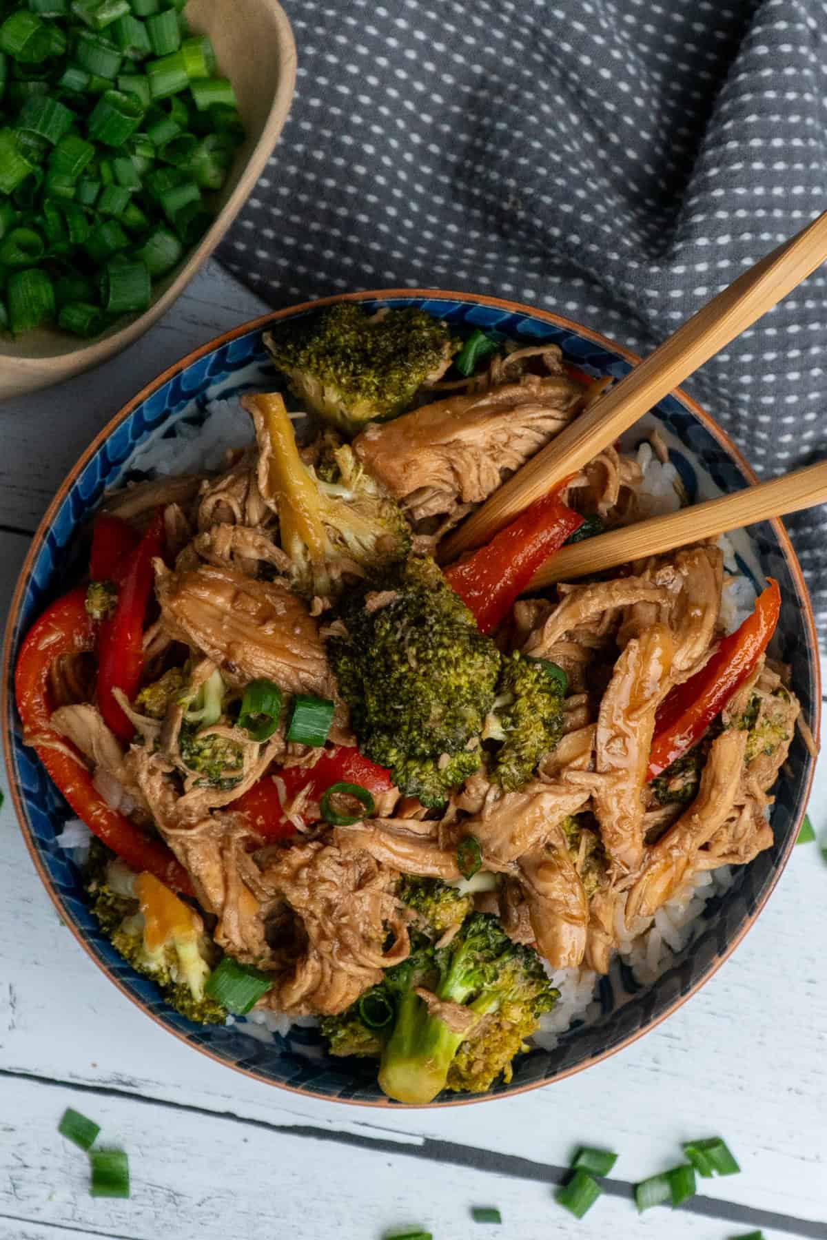 Teriyaki chicken over a bowl of rice with chopsticks in it.