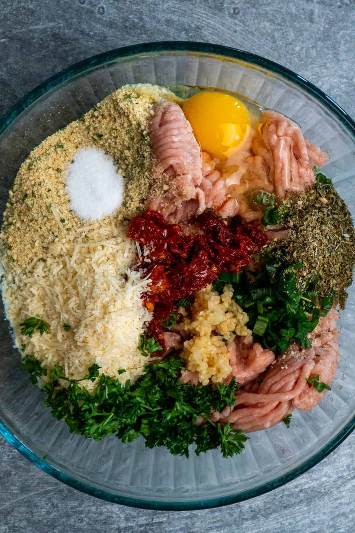 Ingredients to make chicken meatballs in a clear glass bowl.