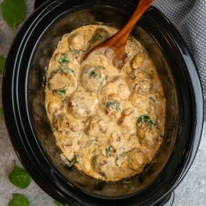 Crock pot Tuscan meatballs with gnocchi and wooden spoon ready to serve.